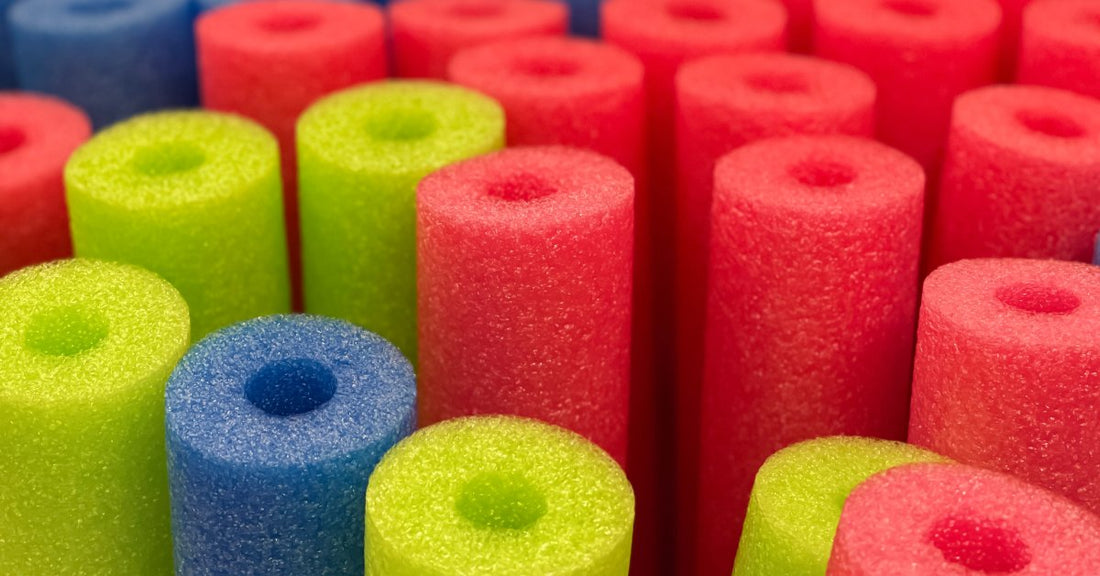 Assorted foam pool noodles in bright red, green, and blue colors arranged closely together, standing upright.