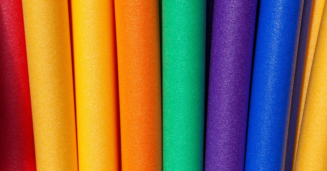 Brightly colored foam pool noodles arranged side by side, featuring vibrant rainbow hues for swimming, floating, and water play.