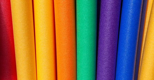 Brightly colored foam pool noodles arranged side by side, featuring vibrant rainbow hues for swimming, floating, and water play.